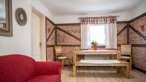 Ein gemütliches Zimmer mit Holztisch, zwei Stühlen, einer roten Couch und einem Fenster mit Vorhängen.