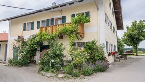 Ein zweistöckiges Gebäude mit einem Balkon, umgeben von verschiedenen blühenden Pflanzen.