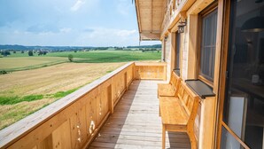 Un balcón de madera con vistas a un campo verde y un pueblo lejano.