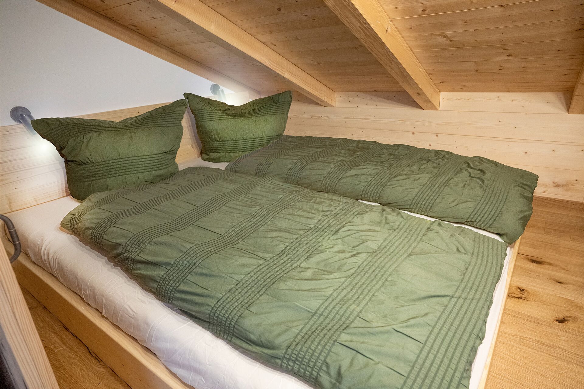 A wooden bed with green bedding in a room with slanted ceilings.