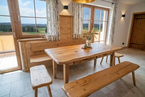 Ein Holztisch mit Bänken, eine Vase mit Trockenpflanzen und Blick auf die Landschaft durch große Fenster.