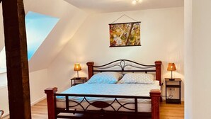 Une chambre à coucher avec un lit, deux tables de chevet, une œuvre d’art suspendue et un plafond en pente.