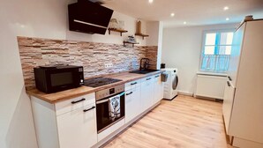 Une cuisine moderne avec un dosseret en pierre, un plan de travail en bois, un four encastré et des meubles de cuisine blancs.