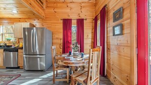 A wooden cabin interior with a kitchen, dining area, and a red door. - Whisper Cabin: Hot Tub, Game Loft, Open Living, Minutes to Downtown Gatlinburg (Gatlinburg)