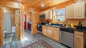 A wooden cabin kitchen with wooden cabinets, a microwave, a sink, and a dishwasher. - Whisper Cabin: Hot Tub, Game Loft, Open Living, Minutes to Downtown Gatlinburg (Gatlinburg)
