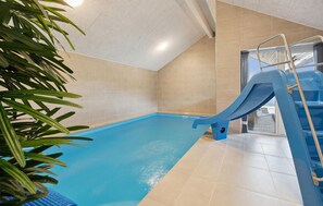 Ein Schwimmbecken mit Rutsche, gefliesten Wänden und einer Deckenleuchte.