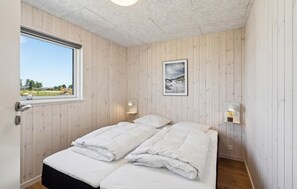 Ein Schlafzimmer mit einer holzgetäfelten Wand, einem Bett mit weißer Bettwäsche, einem gerahmten Bild und einem Fenster mit Blick.