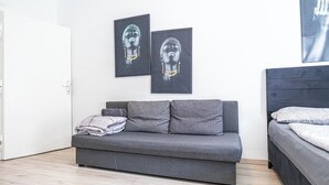 Een moderne slaapkamer met een grijze bank, een bed met beddengoed met een patroon, en twee kunstwerken in lijsten aan de muur.