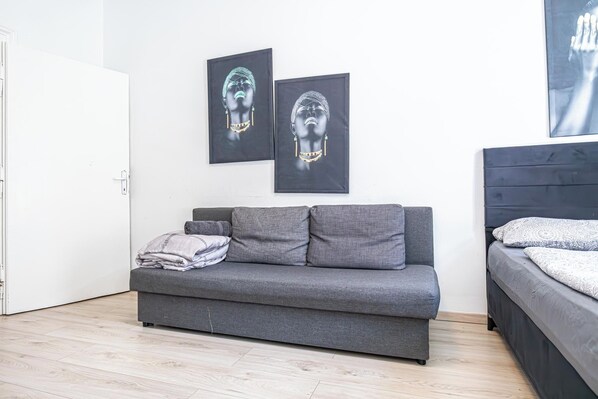 A modern bedroom with a grey sofa, a bed with patterned bedding, and two framed artworks on the wall. - Cozy Budget 2BR Apartment Vienna (Vienna)