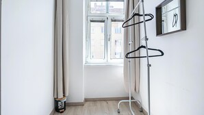 Een kamer met een raam, een metalen rek en een lijst met een afbeelding aan de muur.