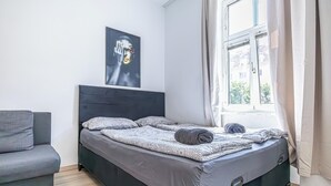 Een moderne slaapkamer met een groot bed, een grijze bank en een raam met gordijnen.