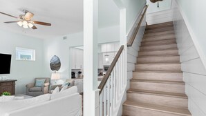 A modern living room with a ceiling fan, a flat-screen TV, and a dining area with a kitchen in the background. - 30A Stay • Golf Cart, Bikes, Outdoor Lounge + Near Beach | Constant Getaway (Santa Rosa Beach)