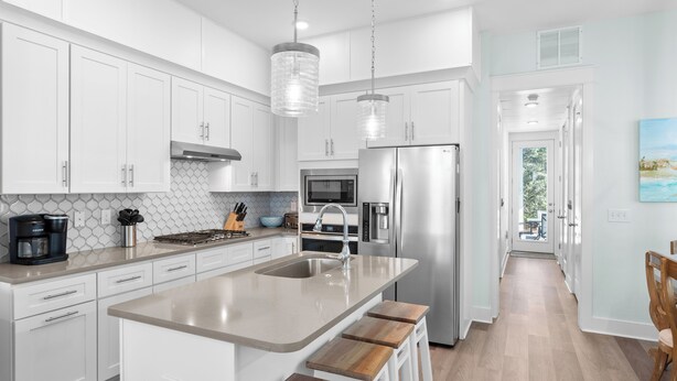 A modern kitchen with white cabinets, stainless steel appliances, and a large island with bar stools. - 30A Stay • Golf Cart, Bikes, Outdoor Lounge + Near Beach | Constant Getaway (Santa Rosa Beach)