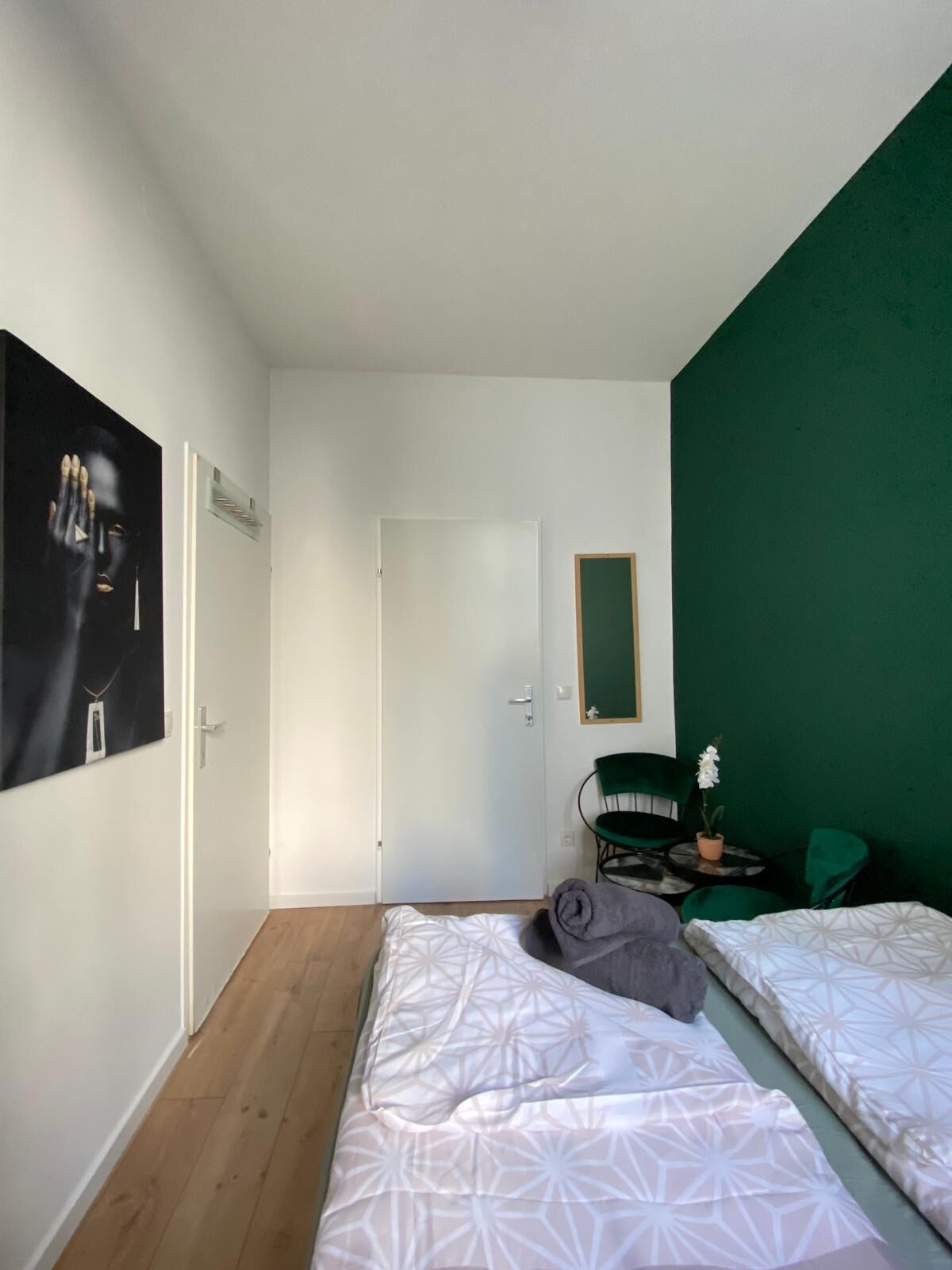 Ein Zimmer mit zwei Betten, einer grünen Wand, einer Tür und einem kleinen Tisch mit einer Pflanze.