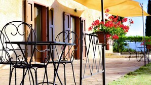 Une terrasse extérieure avec une table et des chaises, un parasol jaune et des pots de fleurs rouges.
