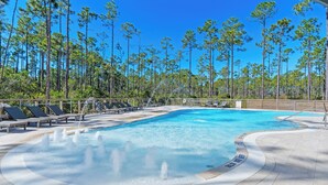 Una piscina con hidromasaje, rodeada de sillas de descanso y altos árboles.