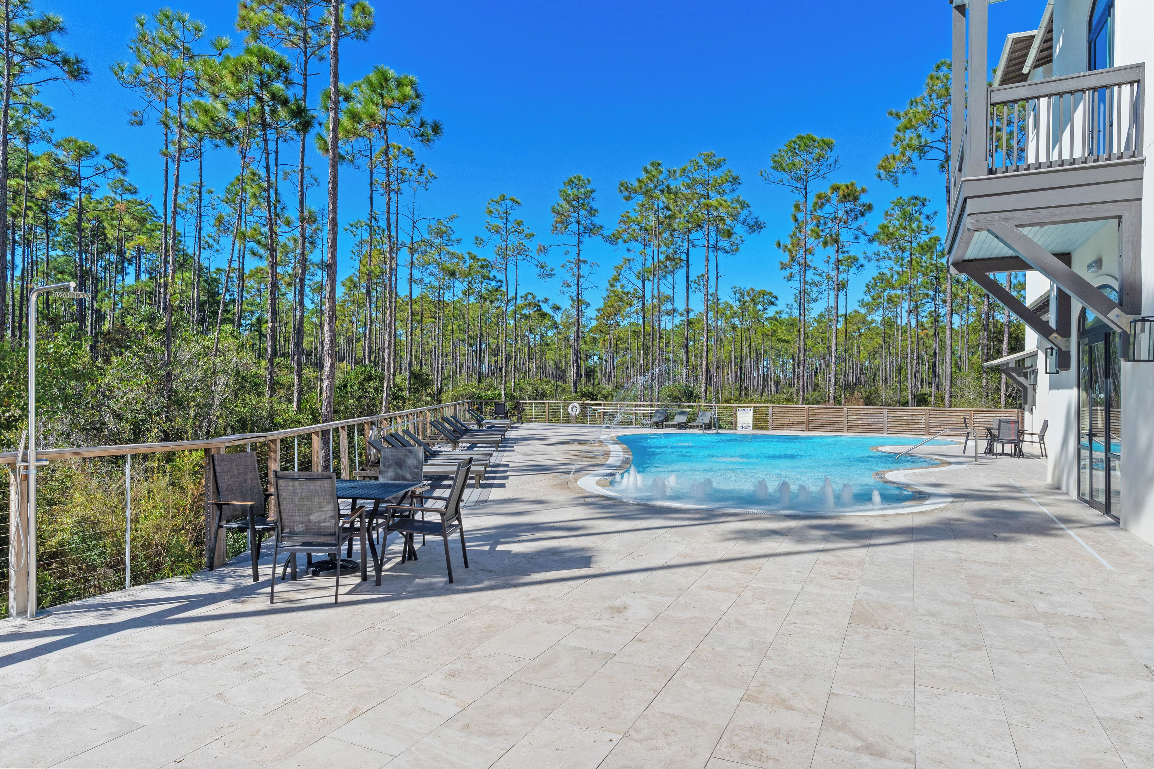 A pool area with lounge chairs and a view of tall pine trees.