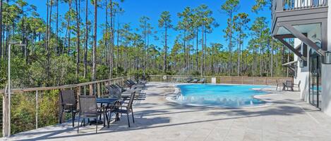 A pool area with lounge chairs and a view of tall pine trees.