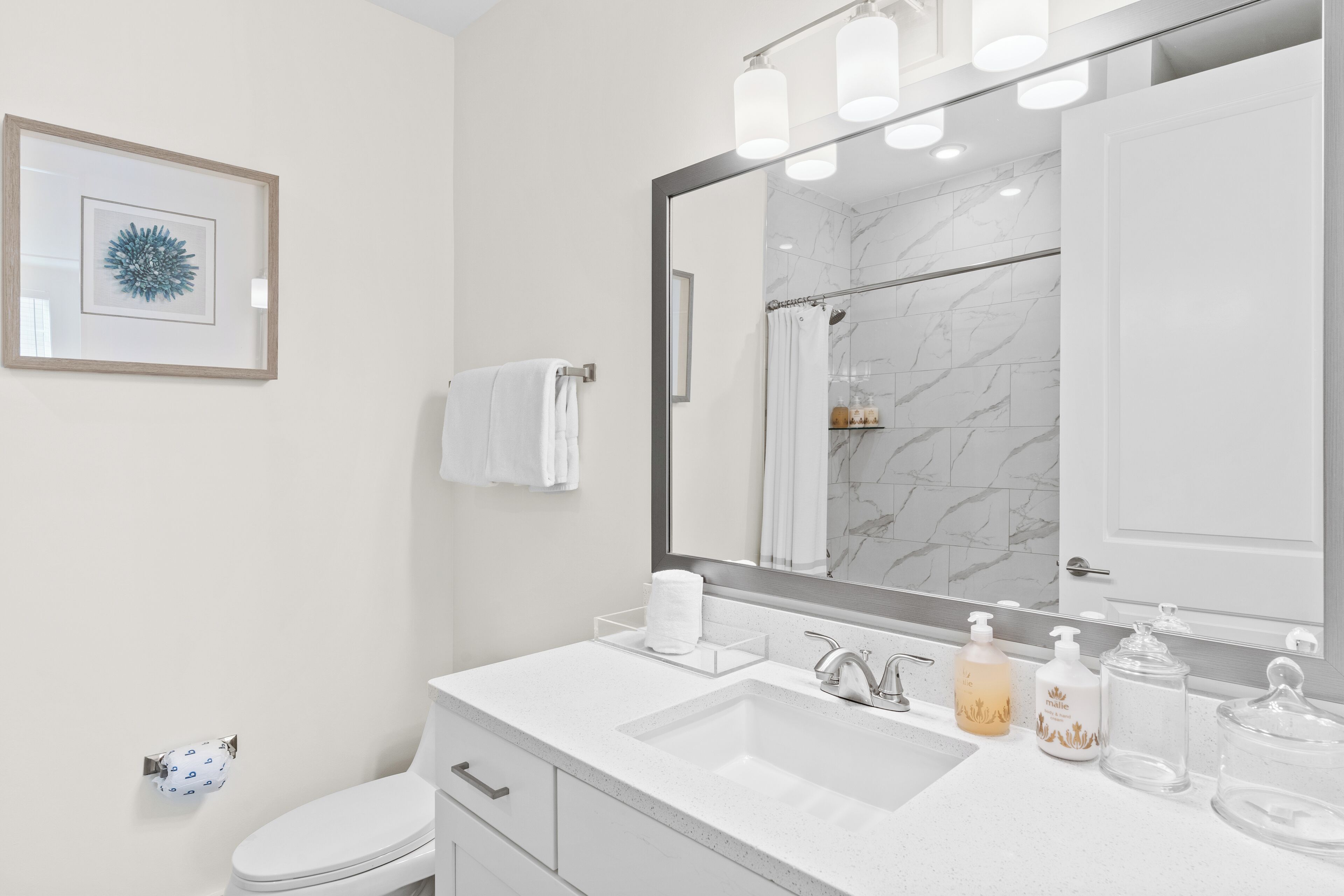 Un bagno moderno con uno specchio grande, un lavandino bianco e una doccia in marmo.