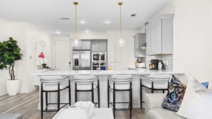 Una cocina moderna con armarios blancos, una isla central con taburetes y luces colgantes.