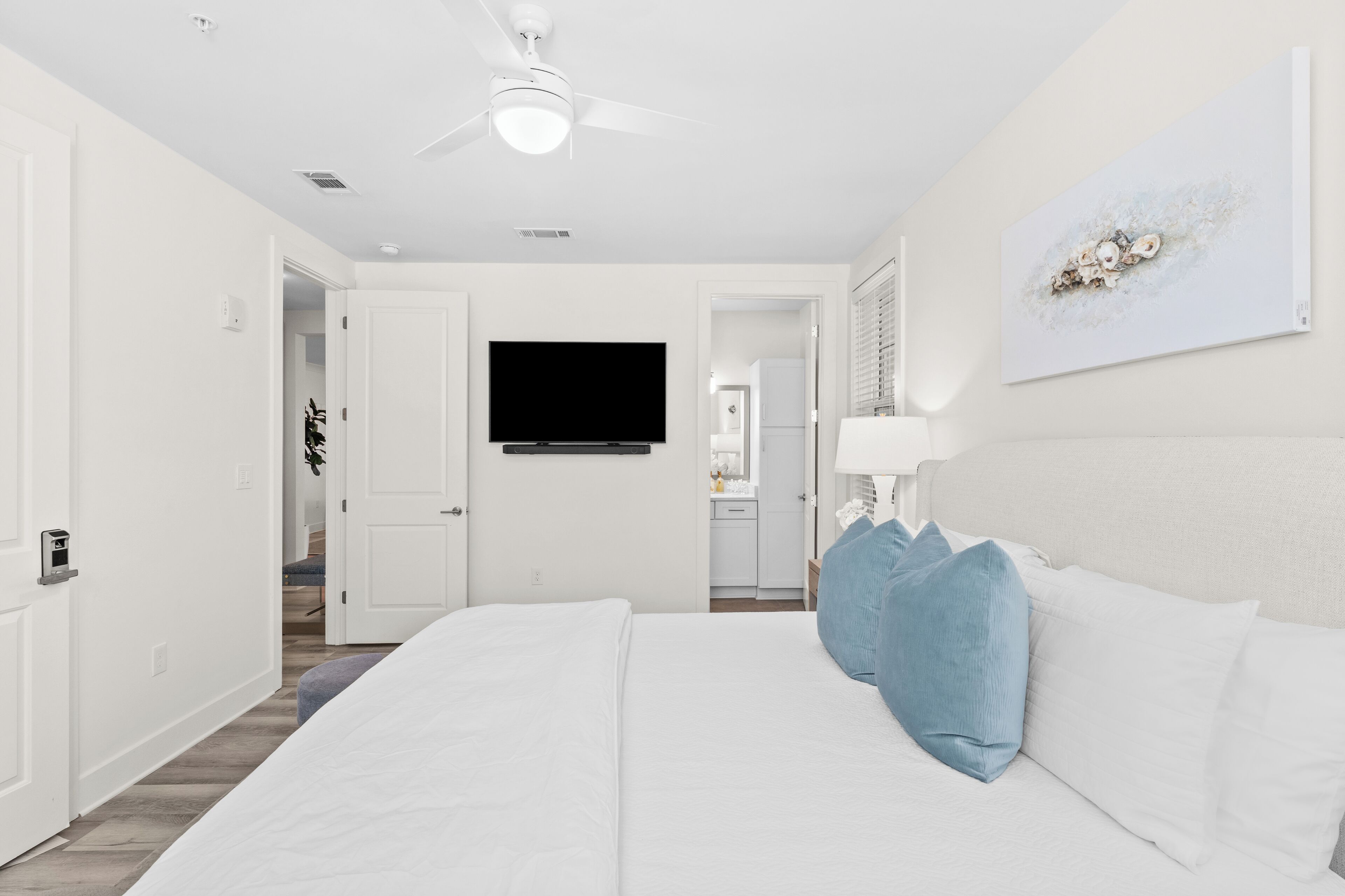 Une chambre d’hôtel moderne avec un grand lit, un ventilateur de plafond, un téléviseur à écran plat et un tableau au mur.