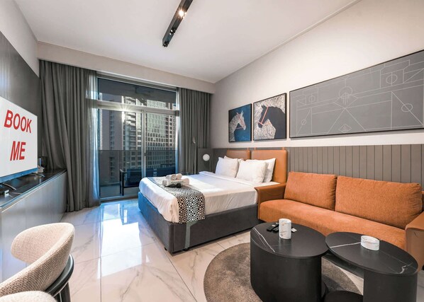 Ein modernes Hotelzimmer mit Bett, Sofa und Schreibtisch mit dem Schild 'BOOK ME'.