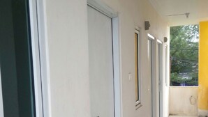 A corridor with white walls and doors, leading to a balcony with a yellow wall and a view of trees. - Penginapan Rumah Kuning Syariah (Bogor)