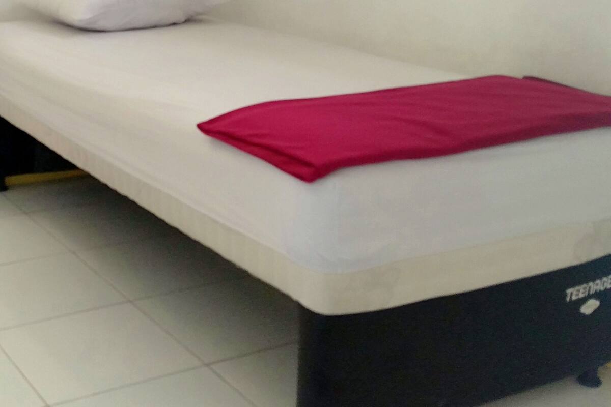 A single bed with a white mattress and a red blanket, a white pillow, and a black headboard with the word "TEENAGE" visible.