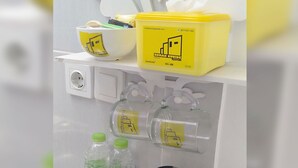A kitchen area with a kettle, two bottles of water, and a yellow container with a logo. - Penginapan Rumah Kuning Syariah (Bogor)
