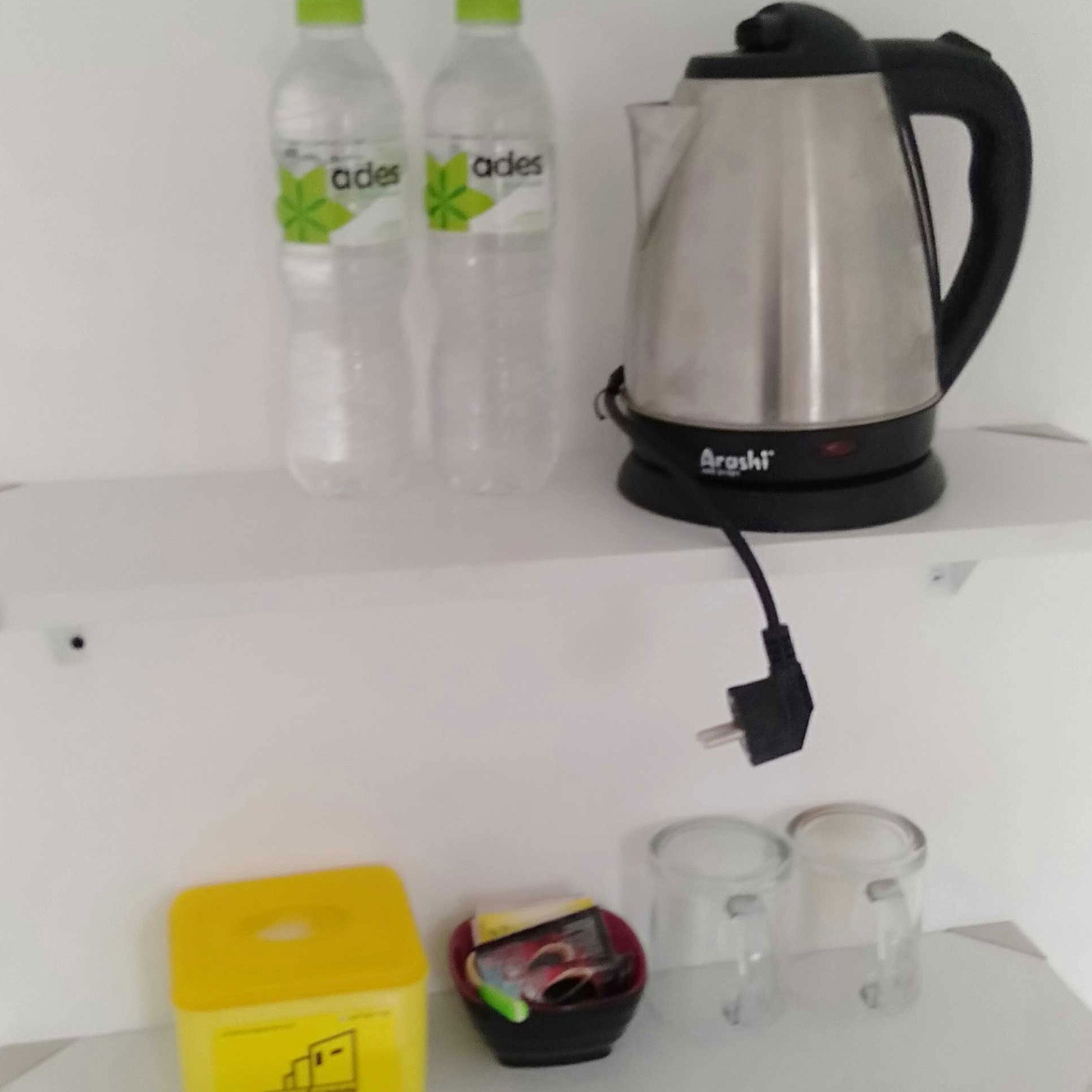 A kitchen area with a kettle, two bottles of water, a yellow container, and two glasses.