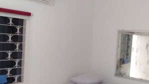 A small, white room with a single bed, a window with bars, and an air conditioning unit on the wall. - Penginapan Rumah Kuning Syariah (Bogor)
