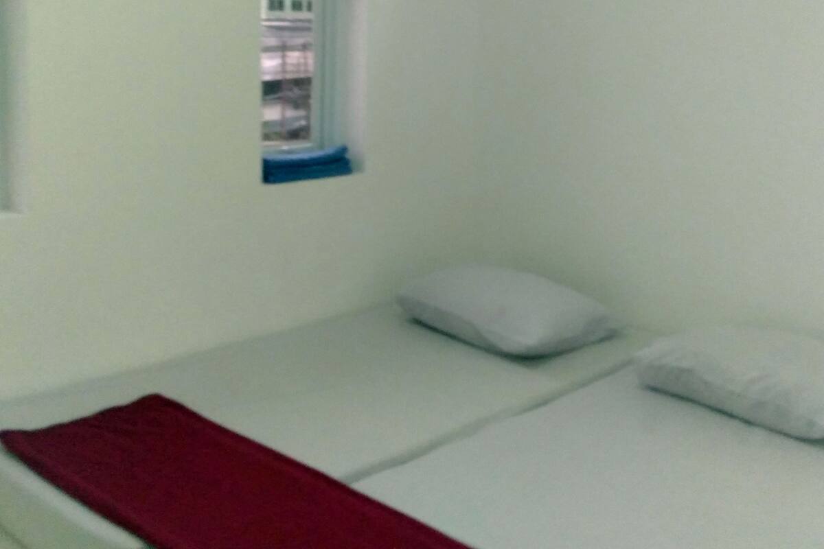 A small, single-bed room with a window, a red blanket, and a white pillow.