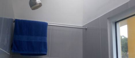 Une salle de bain carrelée de carreaux gris, une serviette bleue suspendue à un porte-serviettes et une fenêtre donnant sur un paysage verdoyant.