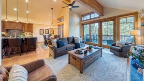 A spacious living area with a large sofa, a coffee table, and a fireplace. There is a dining area with a kitchen in the background. - Truckee Escape w/ Hot Tub, Chef’s Kitchen & Minutes to Skiing, Dining & Trails (Truckee)