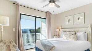 Ein Schlafzimmer mit einem großen Bett, einem Deckenventilator, einem Balkon mit Vorhängen und gerahmten Bildern an der Wand.