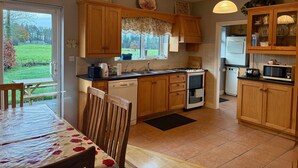A kitchen with wooden cabinets, a dining table with chairs, a window with a view of the outdoors, and a microwave.