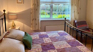 A bedroom with a bed, a bedside lamp, a chair, a window with curtains, and a radiator.