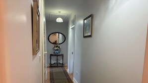 A hallway with a dark green carpet, a mirror on the wall, and a framed picture.