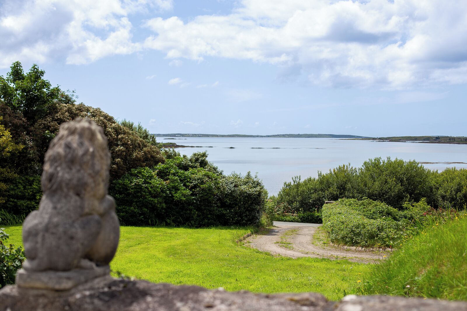 Una escultura de piedra en un área con césped, con un sendero que conduce a una masa de agua.