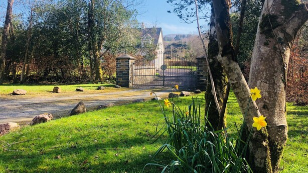 A grassy area with a stone gate, trees, and a distant building. - Birchview Lodge Kenmare (Kenmare)