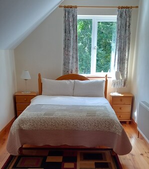 A bedroom with a bed, two nightstands, a window with curtains, and a view of greenery outside. - Birchview Lodge Kenmare (Kenmare)