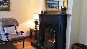 A cozy living room with a fireplace, a comfortable armchair, a small table with a lamp, and a framed picture on the wall. - Birchview Lodge Kenmare (Kenmare)