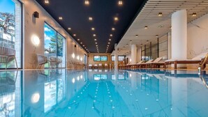 A modern indoor swimming pool with a clear blue floor, large windows, and lounge chairs. - Zlatibor Deluxe Suites with Spa Fitness (Zlatibor)