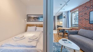 A modern hotel room with a bed, a grey sofa, a small table, and a dining area with a table and chairs. - Zlatibor Deluxe Suites with Spa Fitness (Zlatibor)
