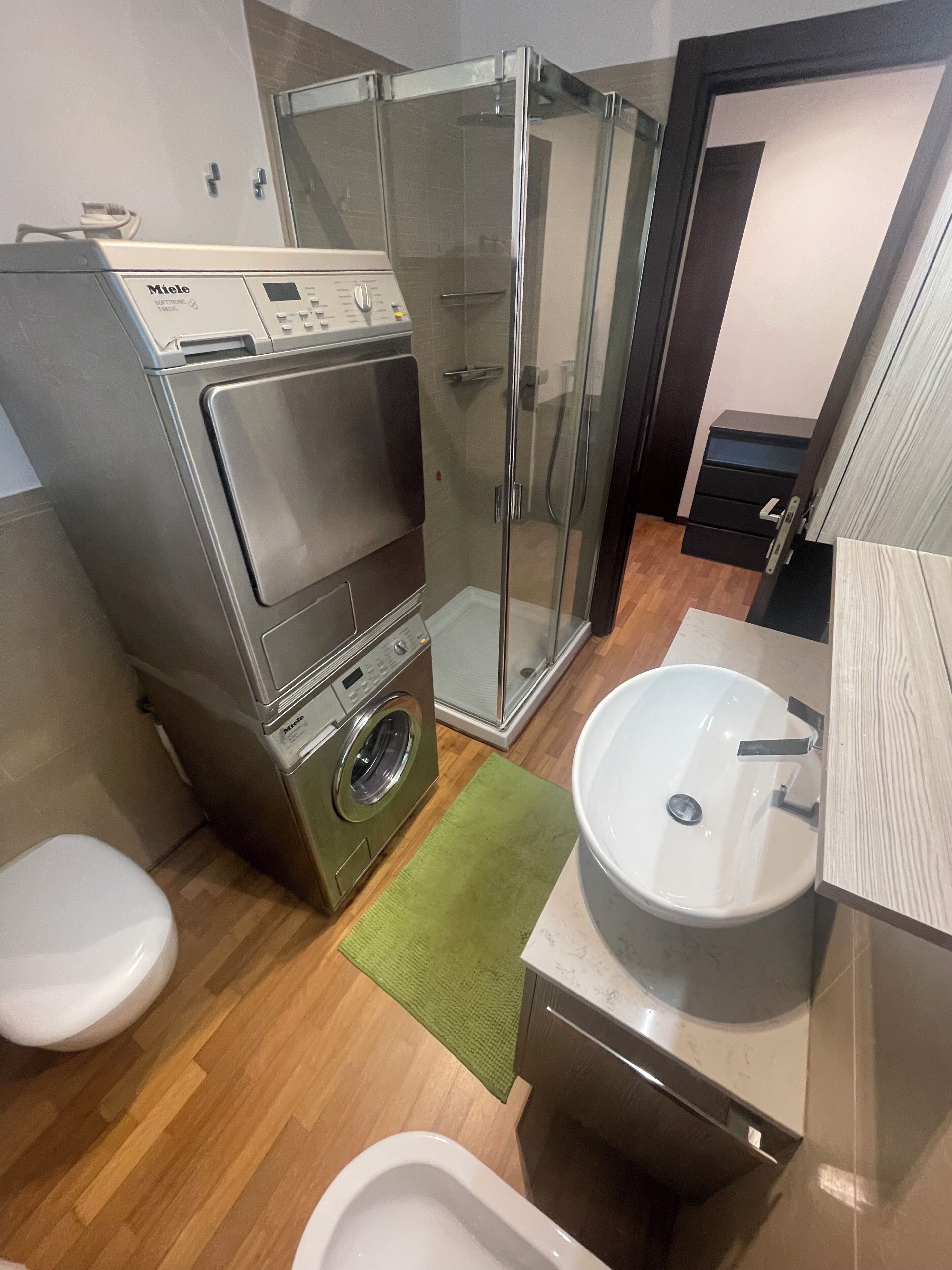 A compact bathroom with a washing machine, a glass-enclosed shower, a sink, and a toilet.