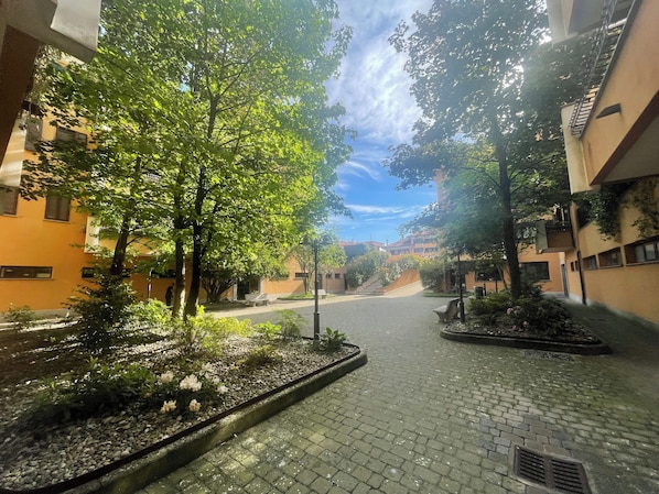 Ein Innenhof mit einem gepflasterten Weg, umgeben von Bäumen und Gebäuden mit Balkonen.