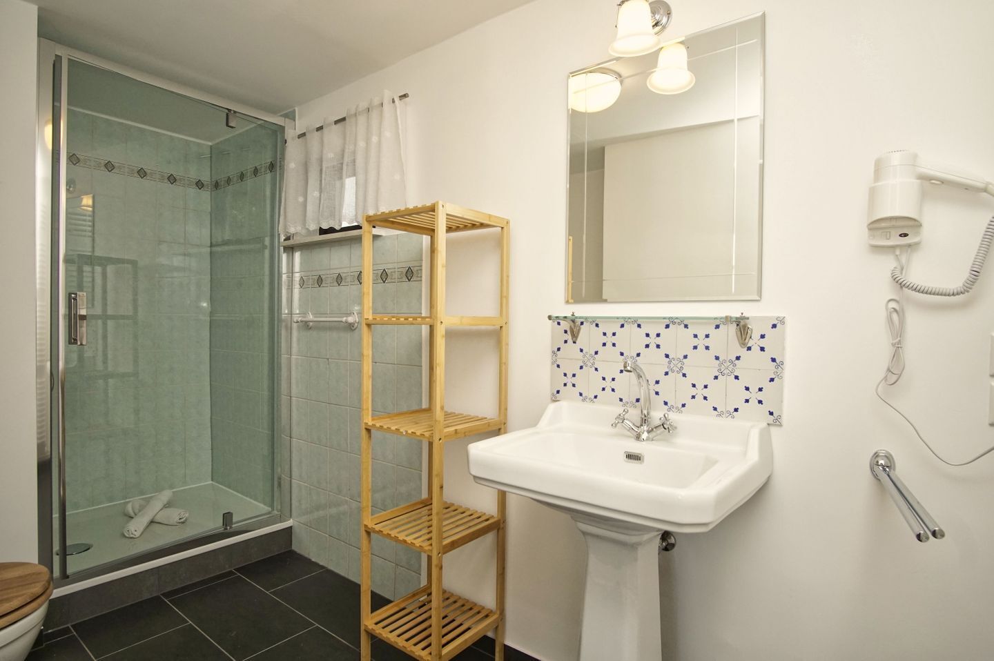 Un baño con cabina de ducha de vidrio, un estante de madera, un lavabo blanco y un espejo con iluminación.