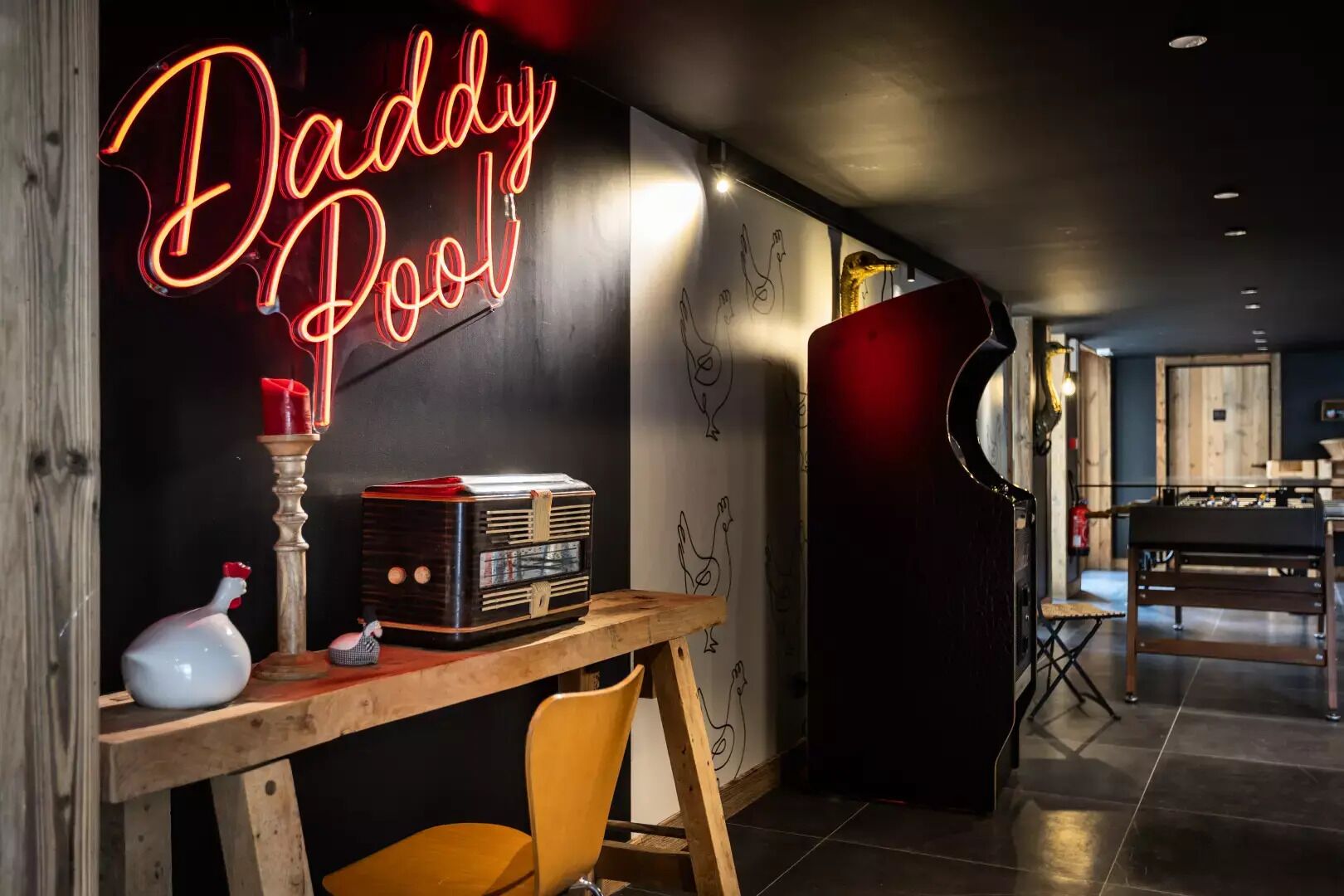 A cozy room with a neon sign reading "Daddy Pool," a vintage radio, and a wooden table.
