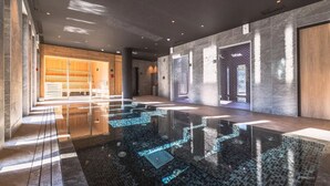 Un'area piscina interna moderna con pavimento in vetro, sedute in legno e un'ampia porta in legno.