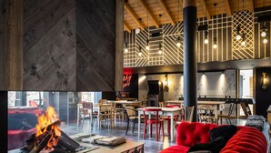 Un ambiente accogliente con camino, sedute rivestite in rosso, tavoli in legno e soffitto a volta con travi a vista.